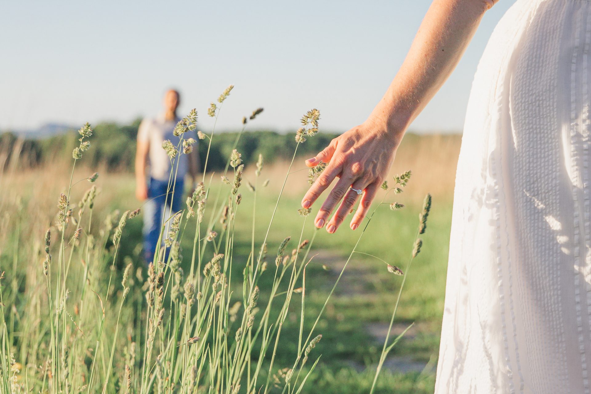 Bride's hand with engagement ring brushing tall grass